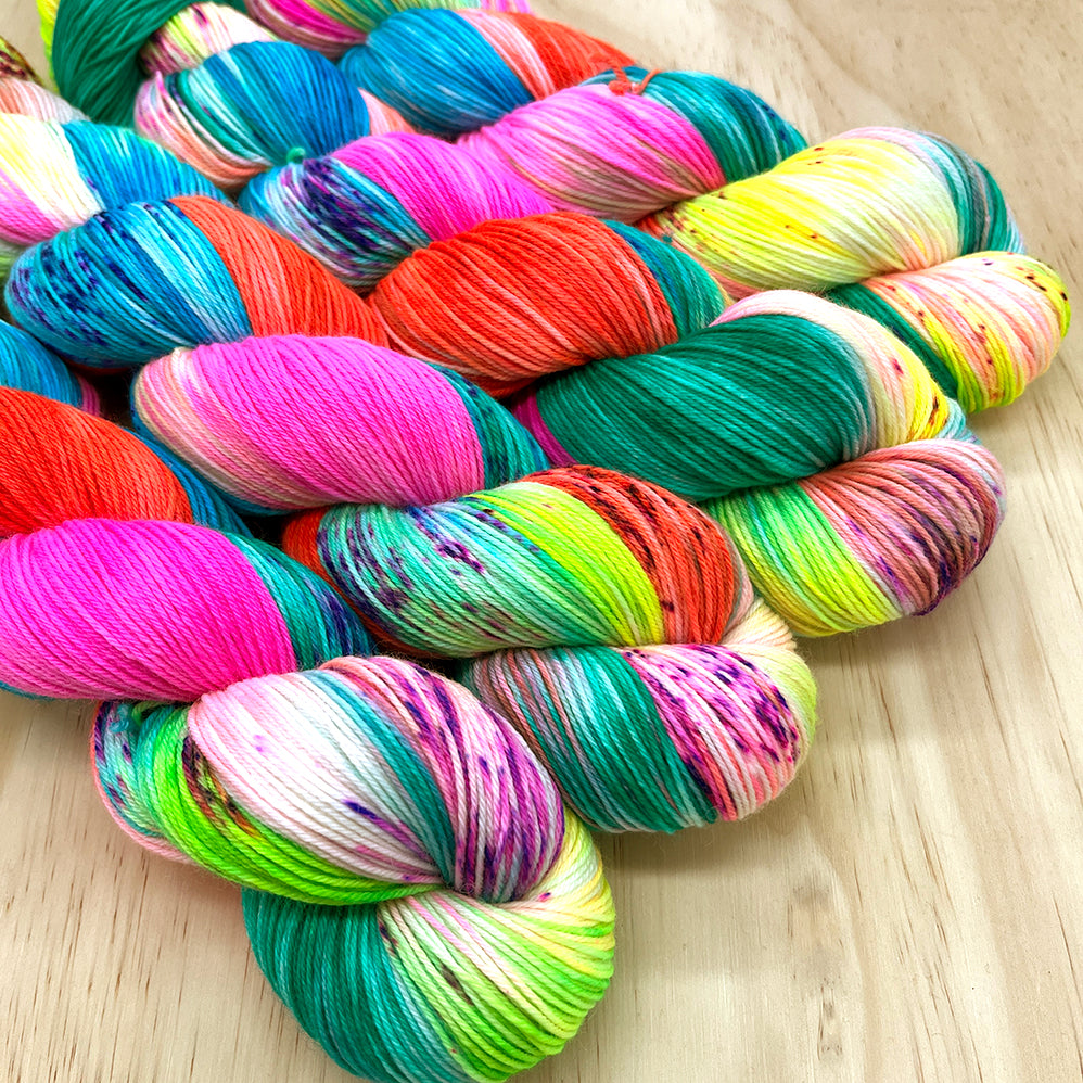 A collection of colorful yarn skeins arranged in a pattern displaying a range of colors including blue, green, orange, pink, and purple with visible speckles of other colors.